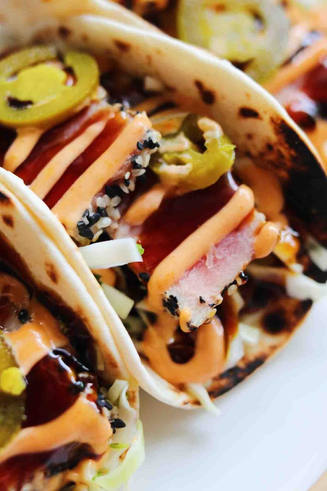 a close up of a folded sesame crusted tuna taco with orange and brown sauce on top.
