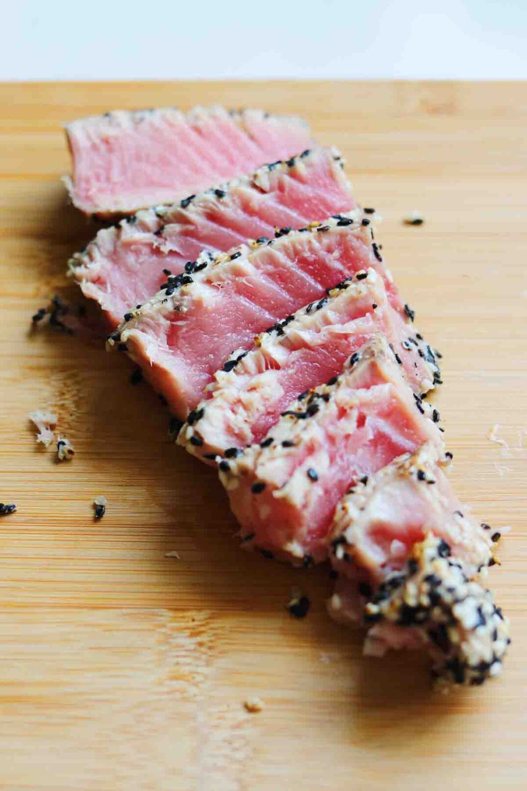 sliced sesame seared tuna on a wooden cutting board.
