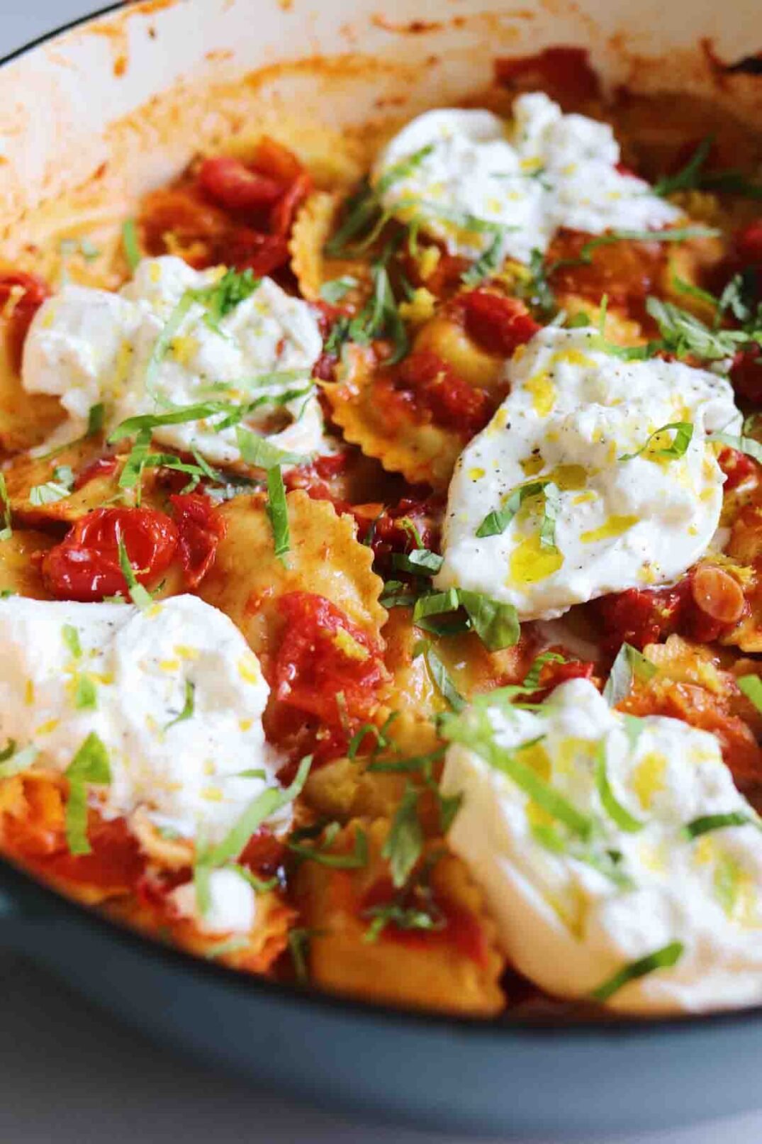 a side angle of a pot of trader joe raviolis in a burst cherty tomato sauce with burrata and basil on top.