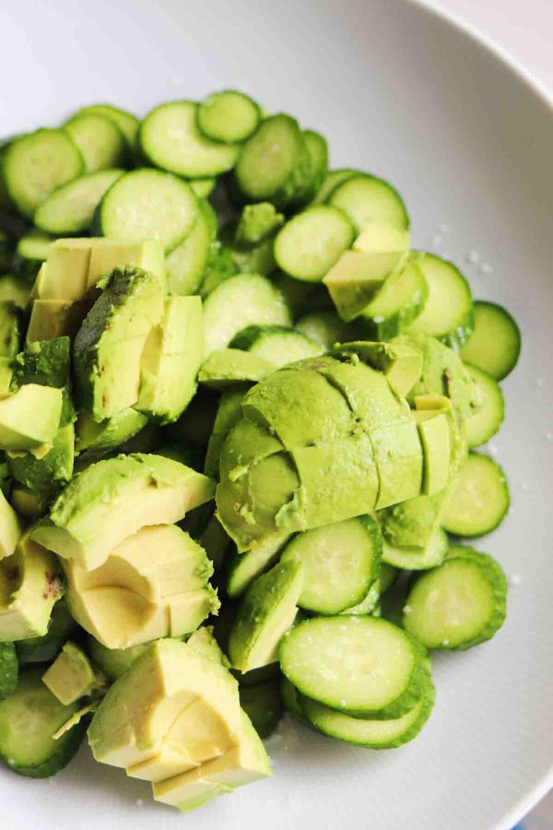 fresh avocado and fresh cucumber chopped up in a white bowl.