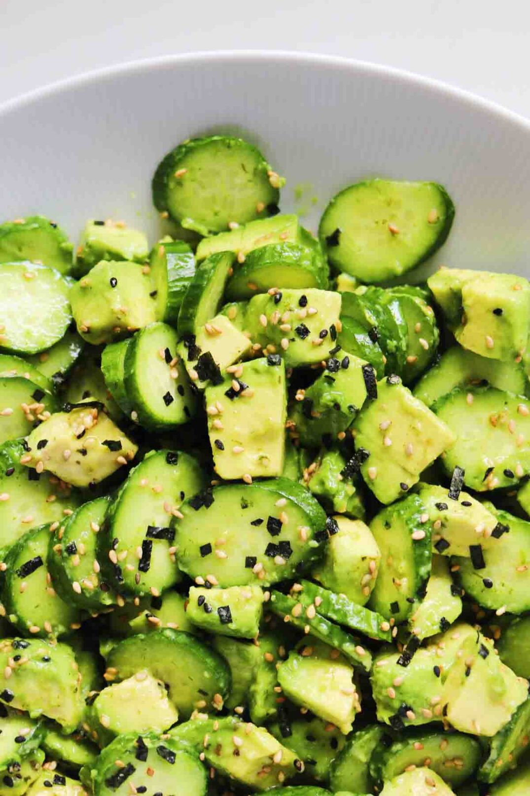 the top of a bowl of avocado and cucumber salad with asian furikake