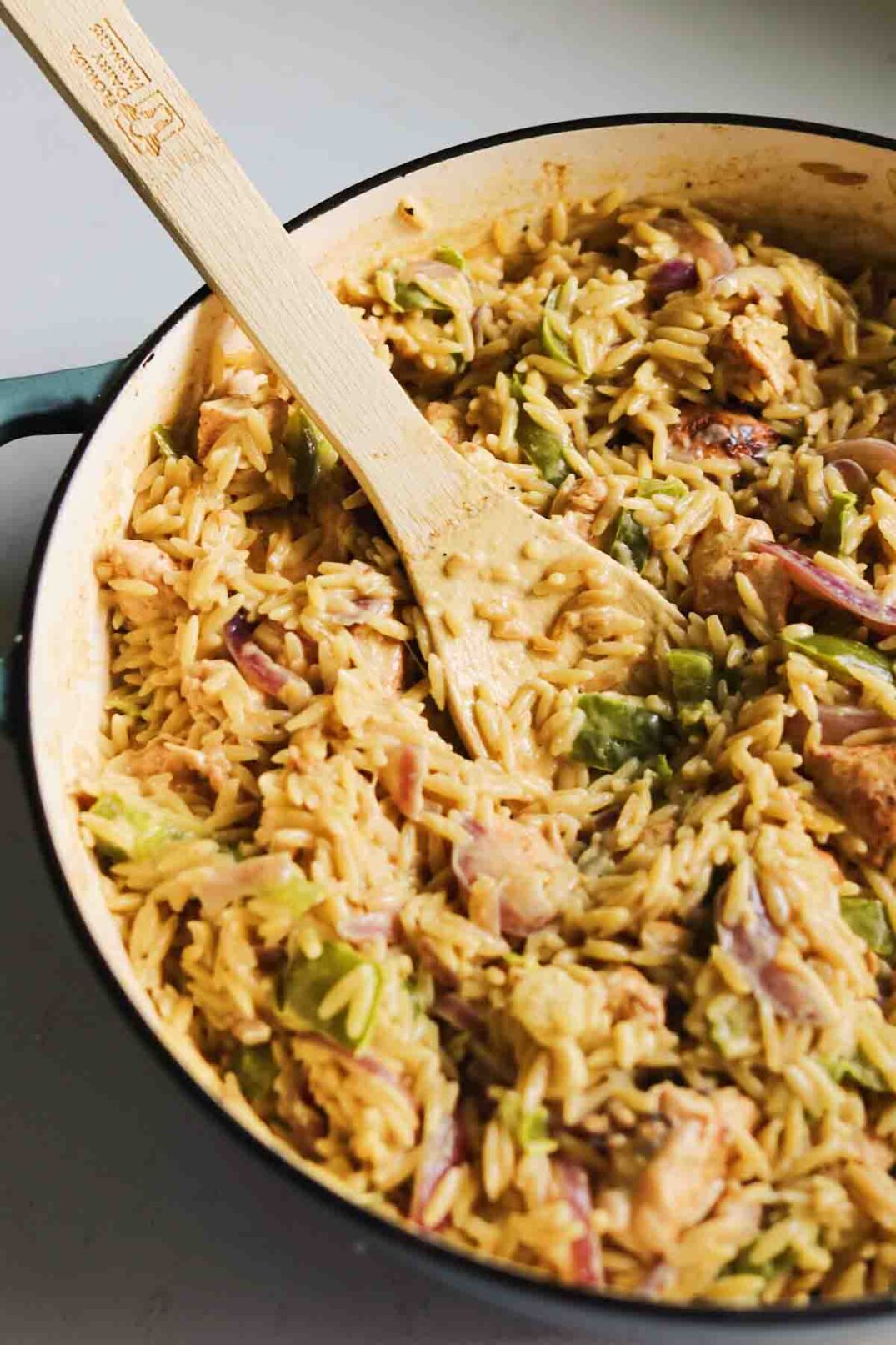 a big pot of cajun chicken orzo with a wooden spoon in it.