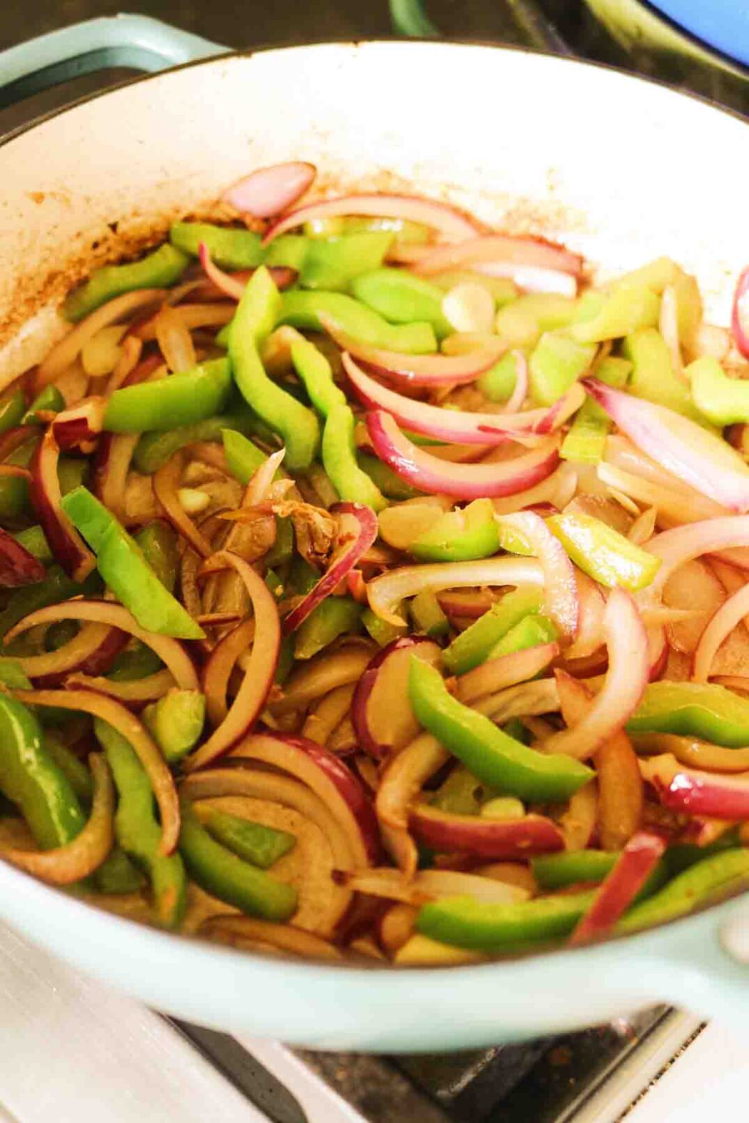 sauteed red onions and green bell peppers cooking together in an enameled cast iron.