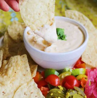 cottage cheese queso in a white bowl surrounded by colorful toppings and tan tortilla chips.