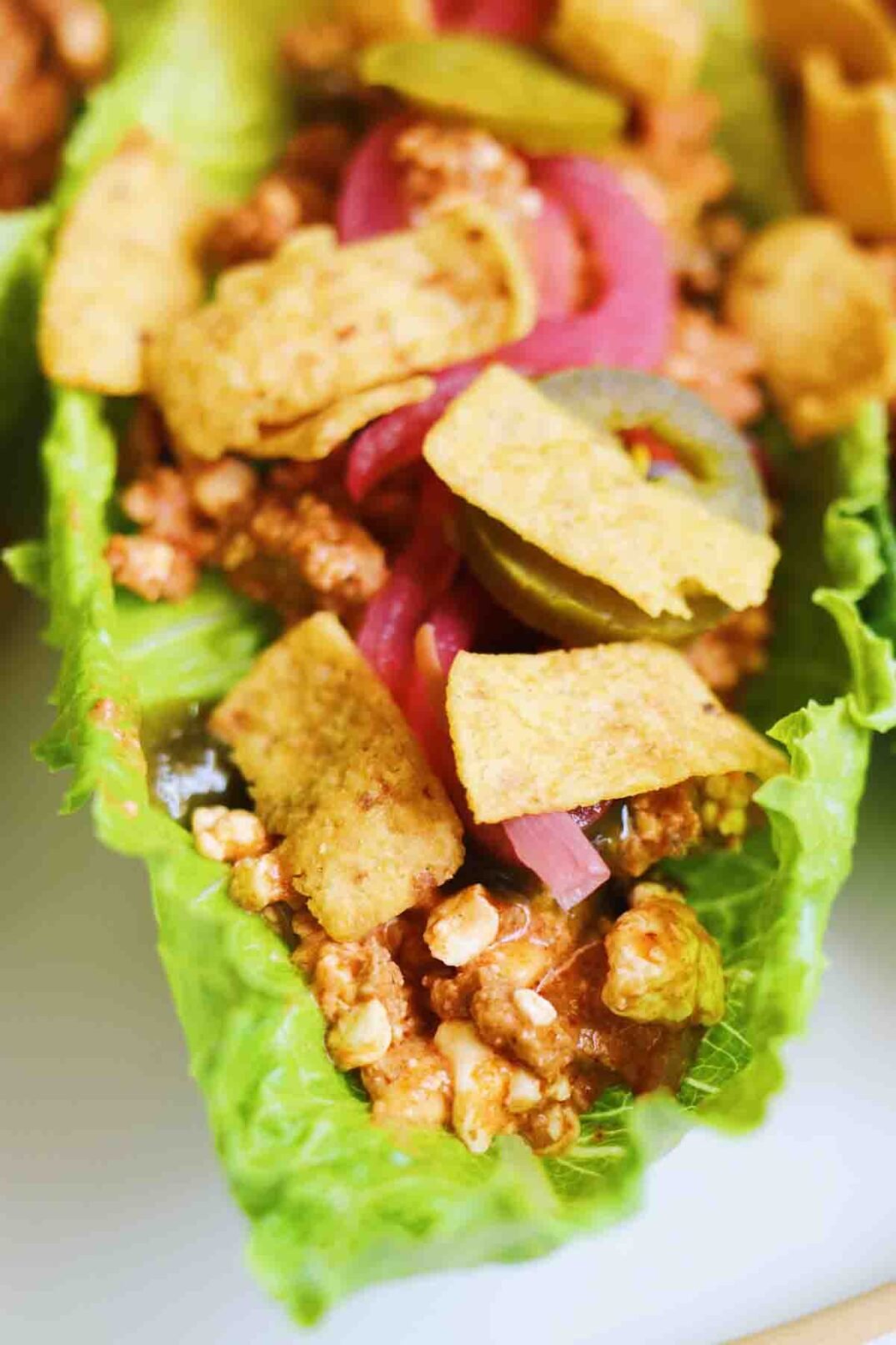 an up close view of a piece of lettuce stuffed with taco meat and cottage cheese and colorful toppings.