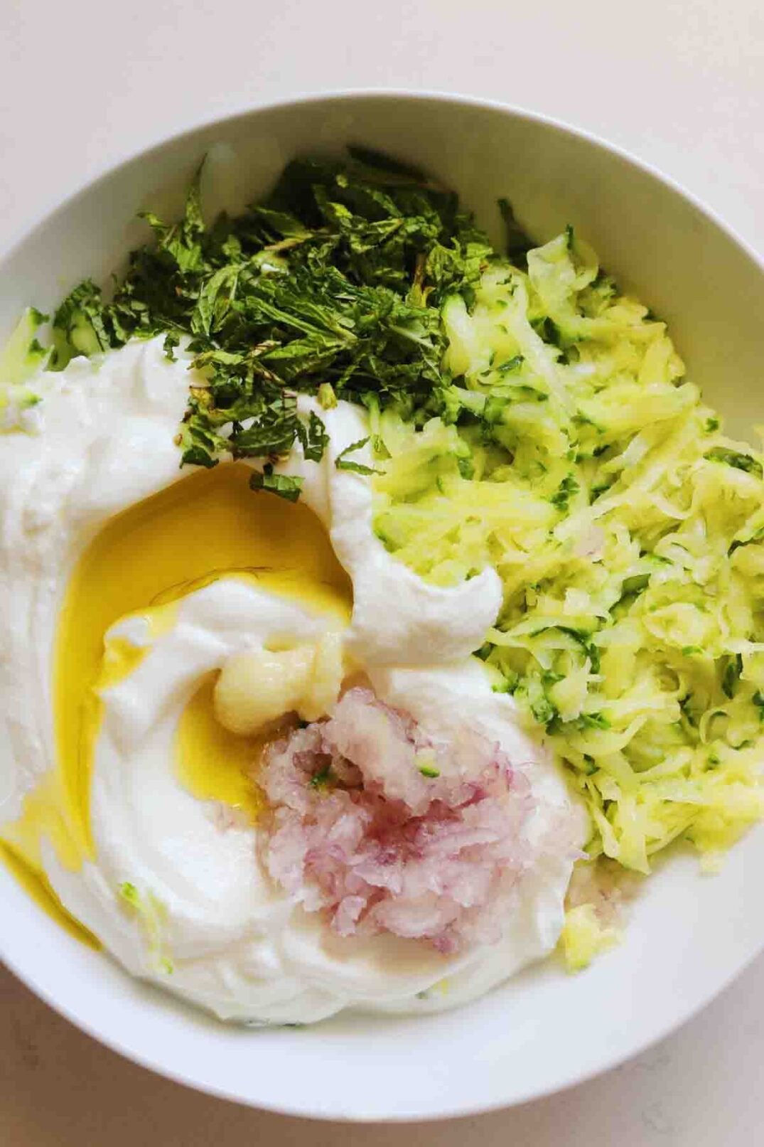 green herbs, pink shallot, white yogurt and yellow olive oil in a white bowl.