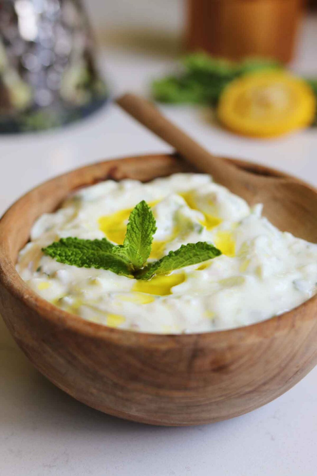 white sauce in a brown wooden bowl with a lemon and mint sprig in the background.
