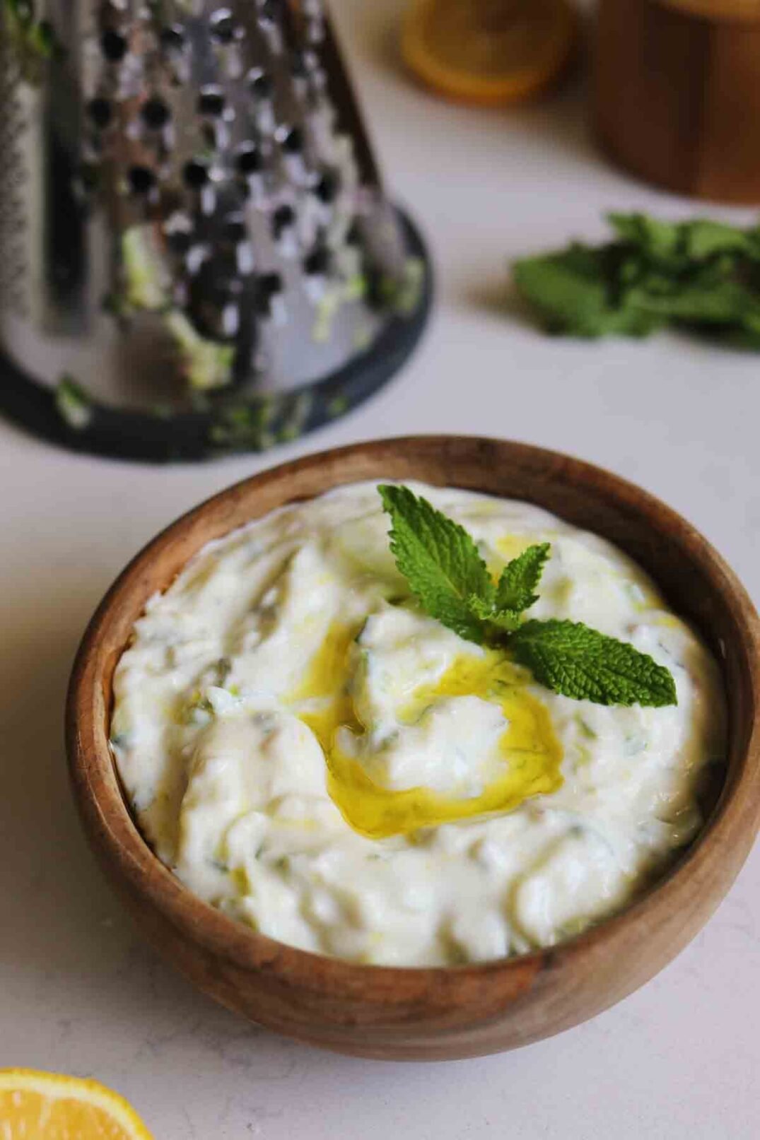white tzatziki sauce in a brown bowl with a grater in the background.