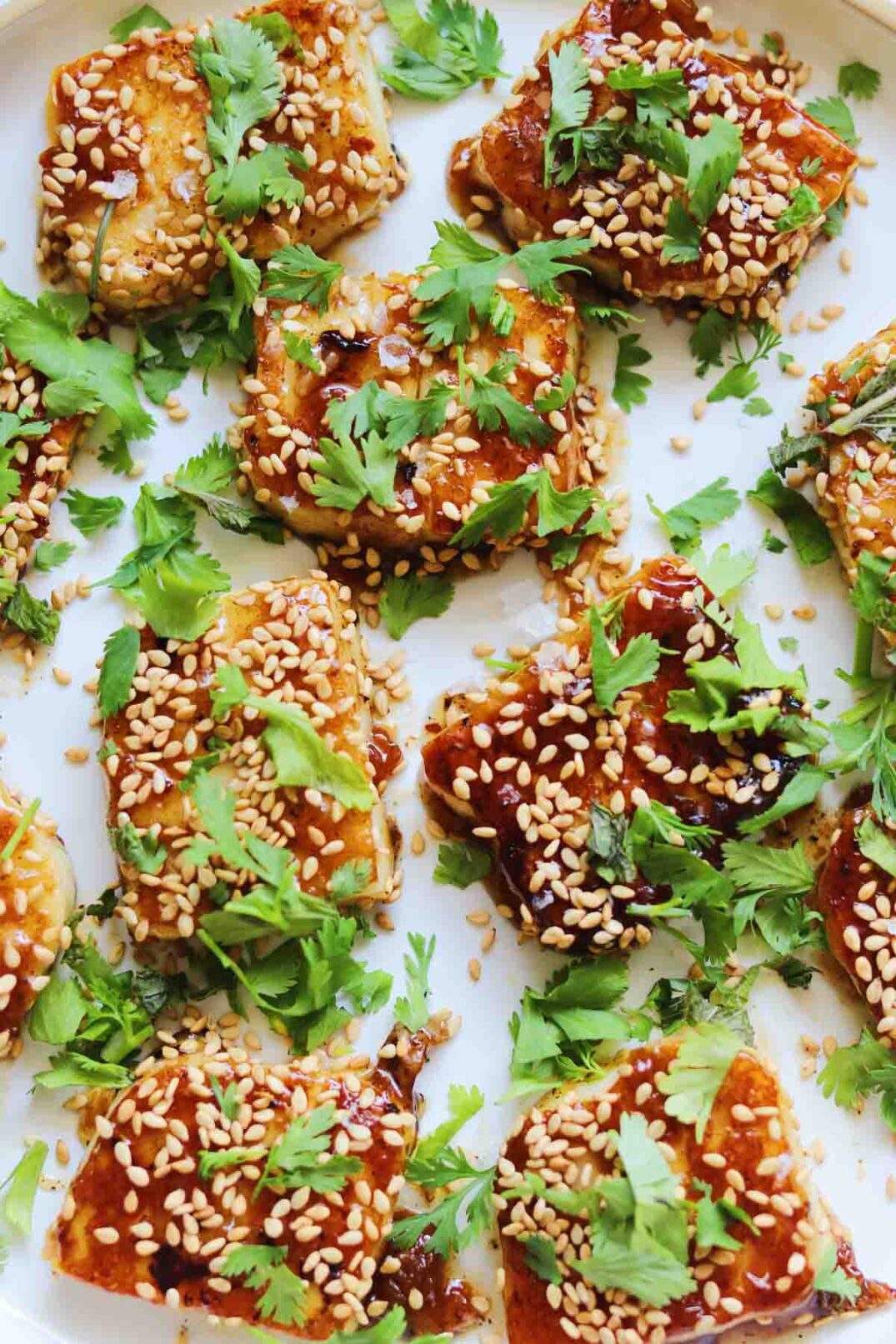 a plate of fried halloumi bites with sesame seeds and fresh herbs.