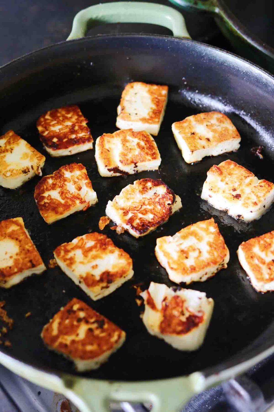 golden brown pieces of halloum in a pan after they've been fried.