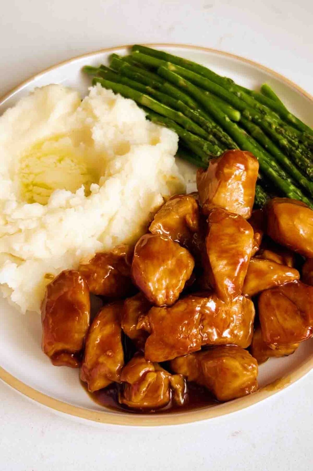 a plate of honey bourbon chicken, mashed potatoes and asparagus. 