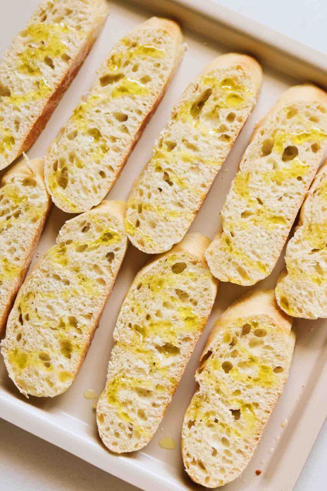 baguette rounds on a baking sheet drizzled with yellow olive oil.