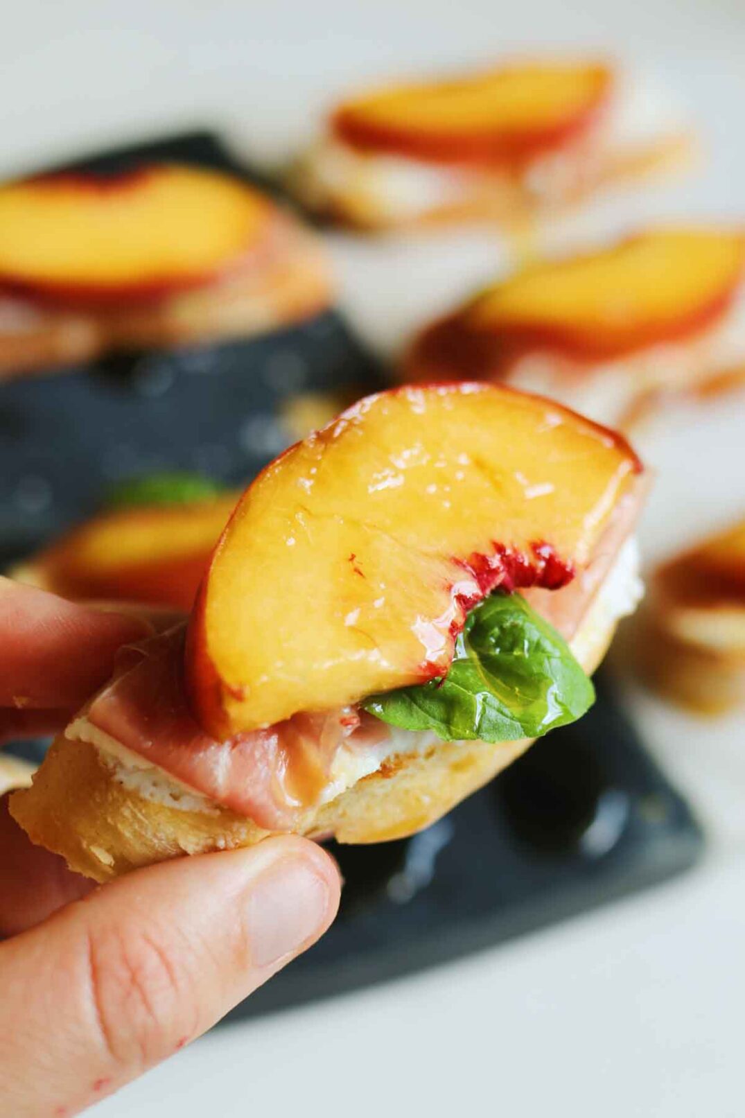 a hand holding a piece of peach and ricotta crostini.