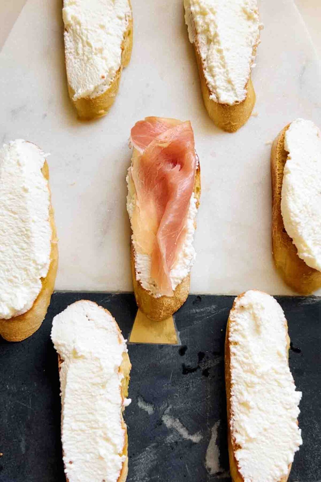 a piece of prosciutto laying on top of a piece of baguette topped with ricotta cheese.