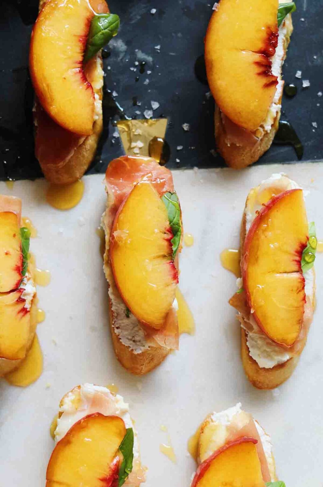 an overhead view of a platter of ricotta crostini with peaches, hot honey and basil.