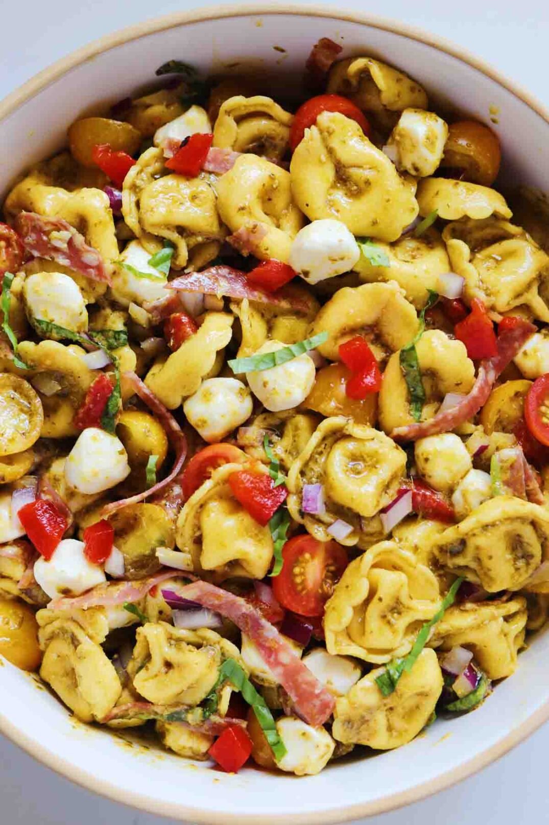 an overhead view of a bowl of pesto tortellini salad on a white countertop.