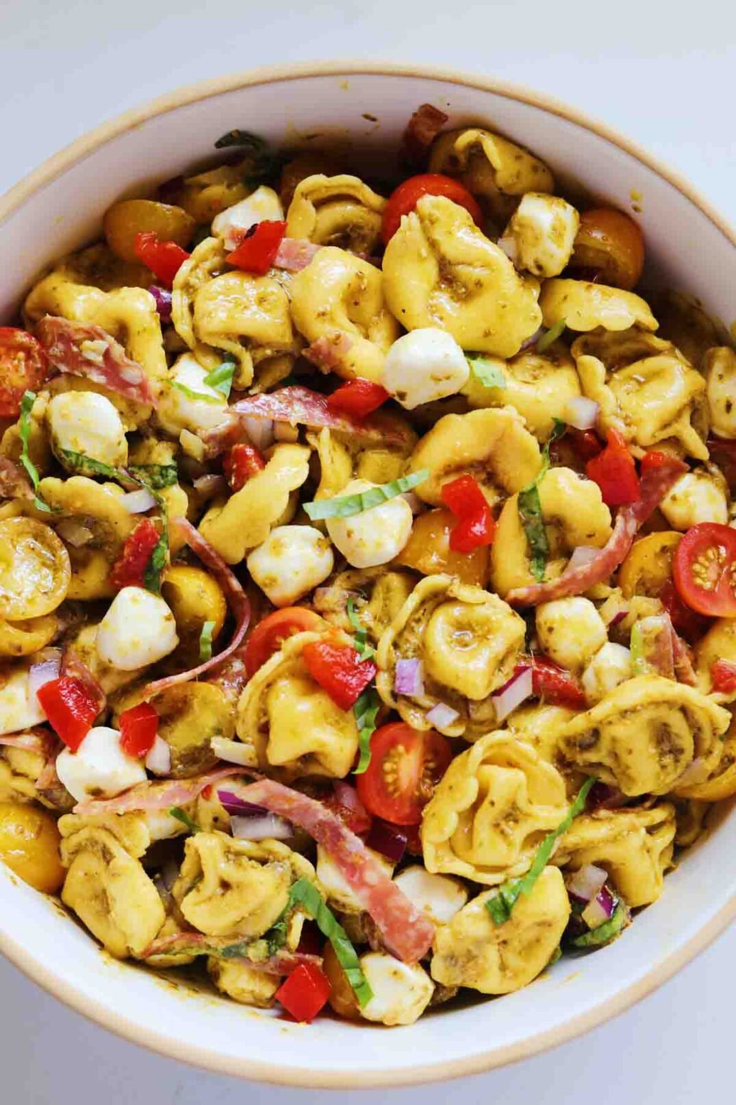 a big bowl of bright green pesto tortellini salad with fresh colorful chopped veggies in a white bowl.