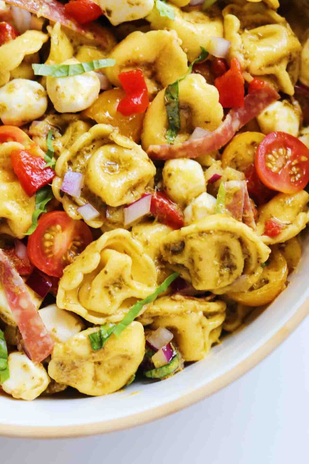 the side of a big white bowl full of colorful chopped veggies, cheese tortellini and. pesto vinaigrette.