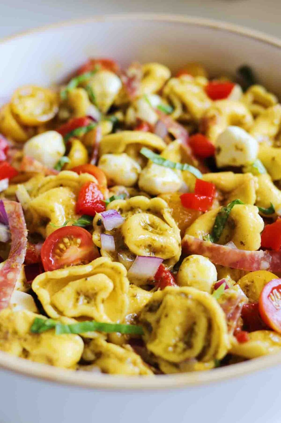 colorful pesto tortellini salad in a white bowl.