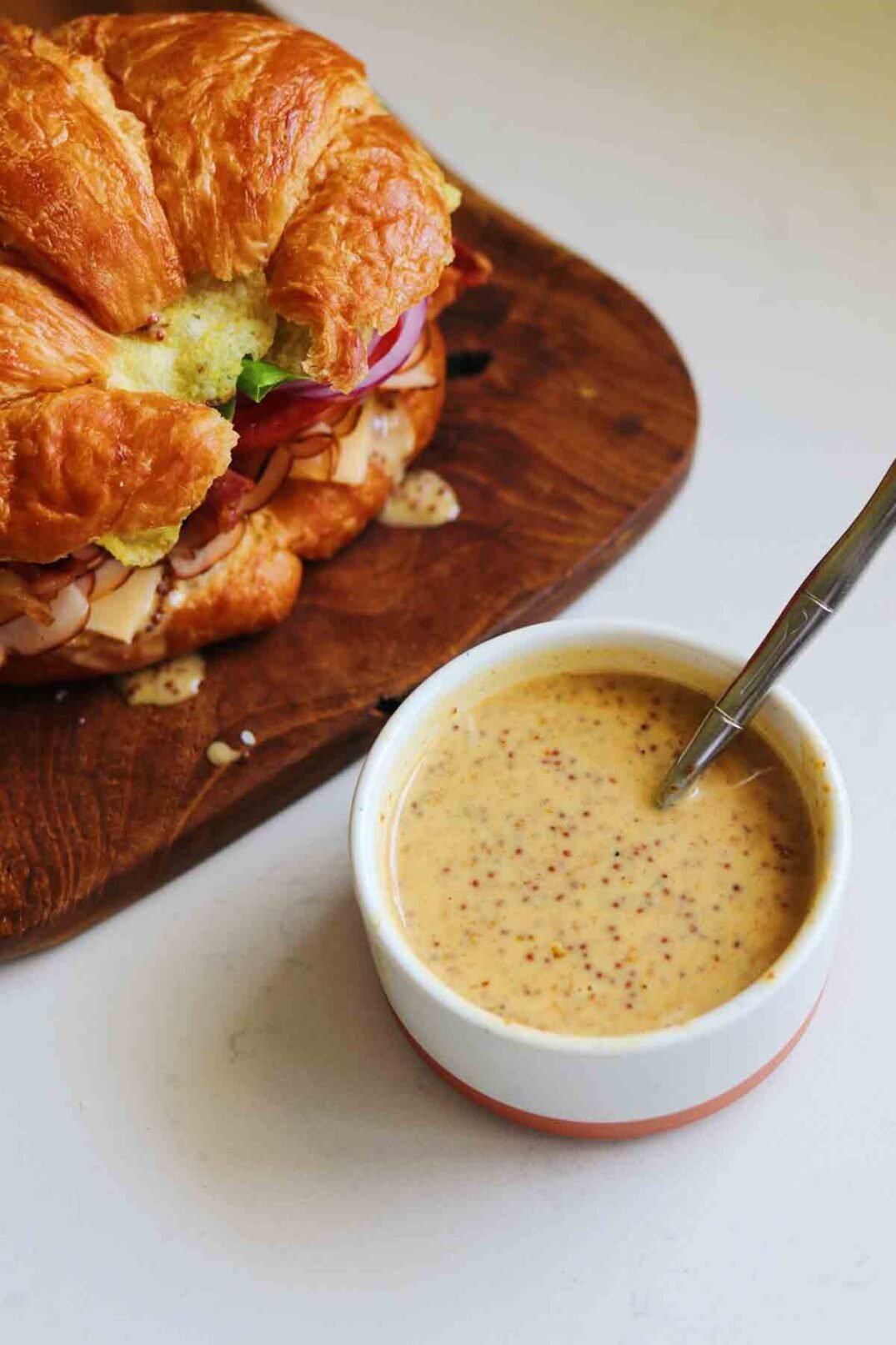 a turkey croissant sandwich with a small bowl of grainy honey mustard.