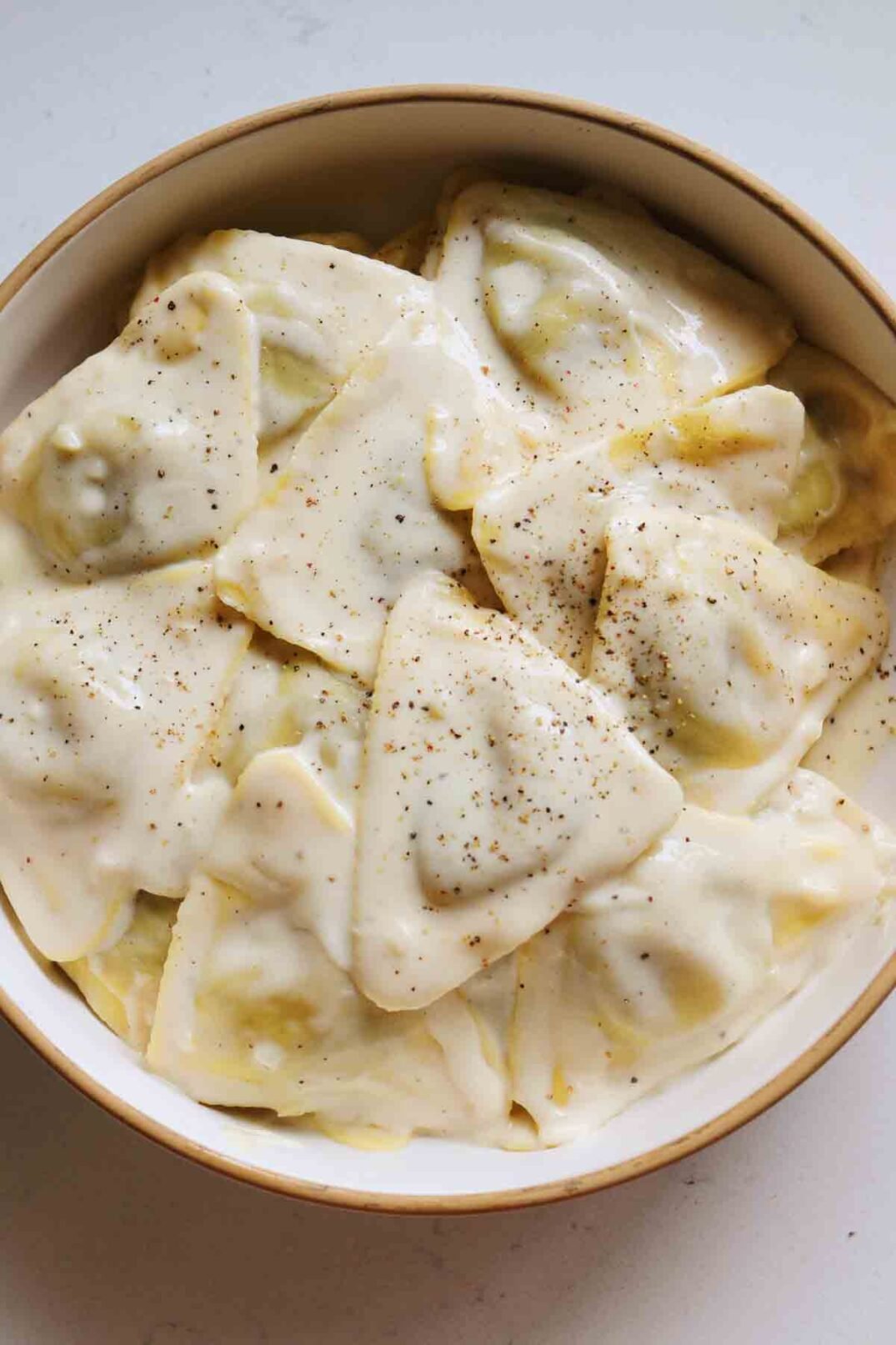 a white bowl on a white countertop filled with Trader Joe's Porcini Mushroom Ravioli  with Truffle Cream Sauce. 