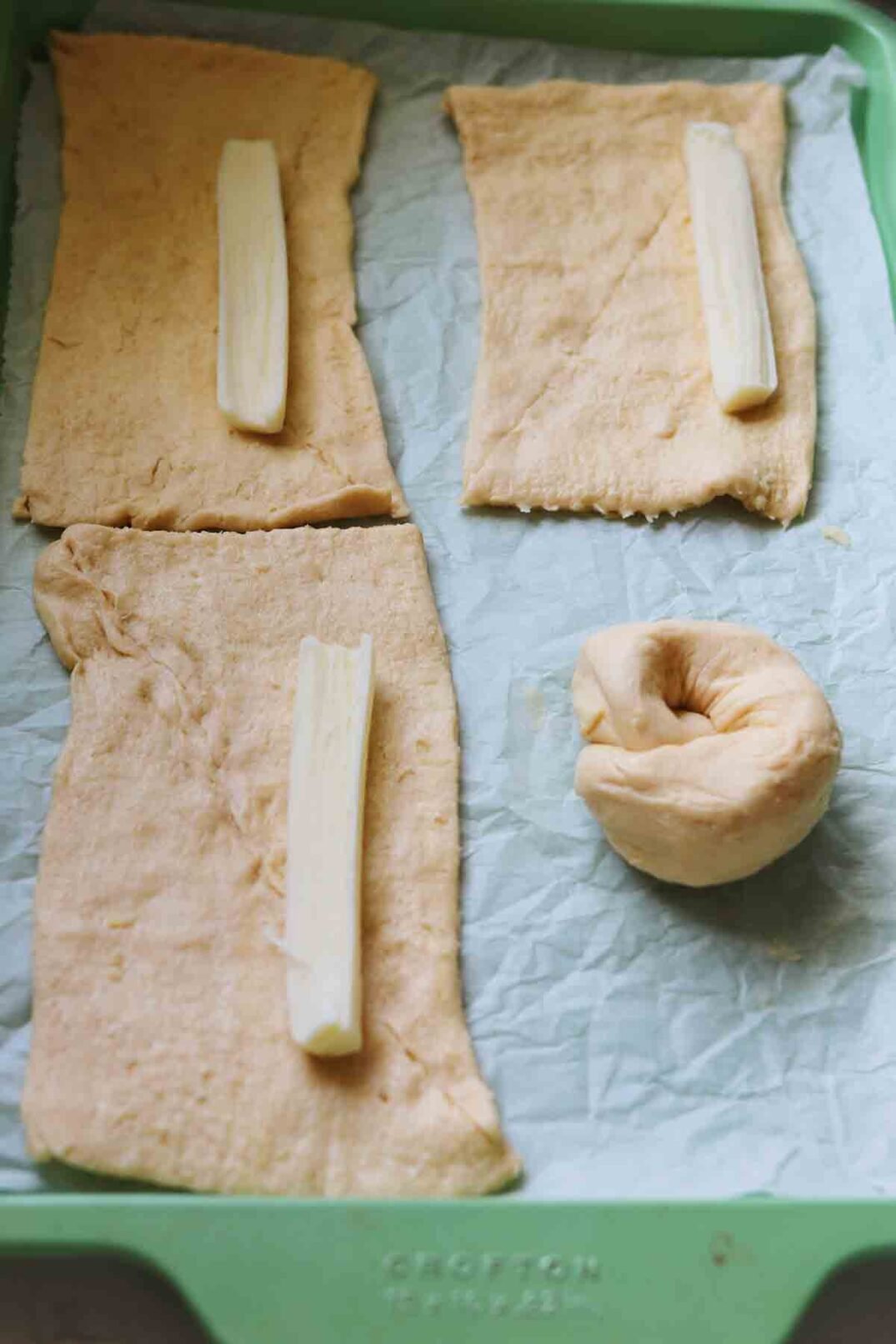 crescent dough rectangles on a baking sheet with a mozzarella stick on top.