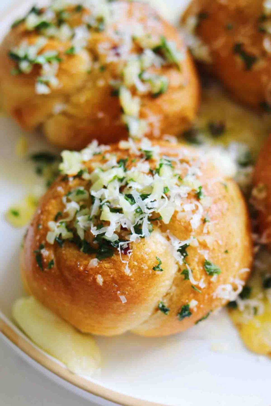 one beautiful garlic knot on a white plate with cheese, garlic bits and parsley.