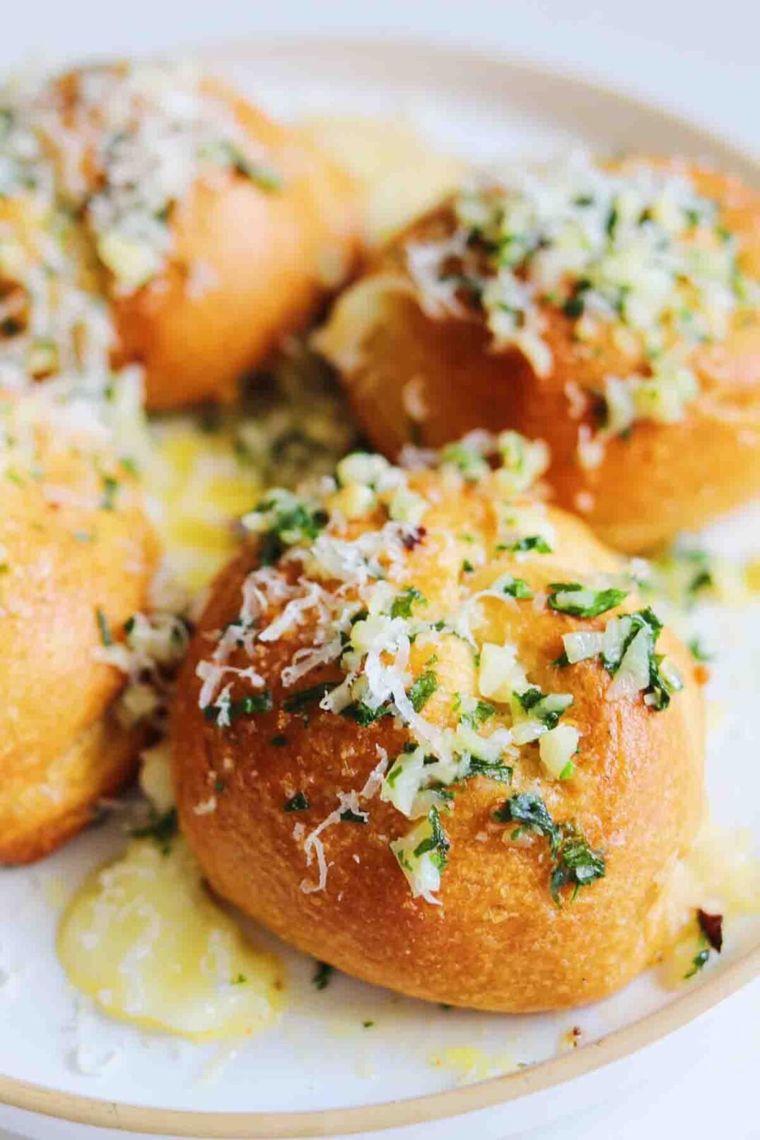 a white plate topped with garlick butter drenched garlic knots with cheese pooling out.