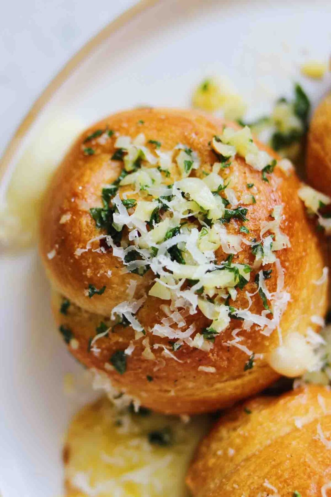 a single Crescent Roll Garlic Knot on a white plate with butter dripping off.