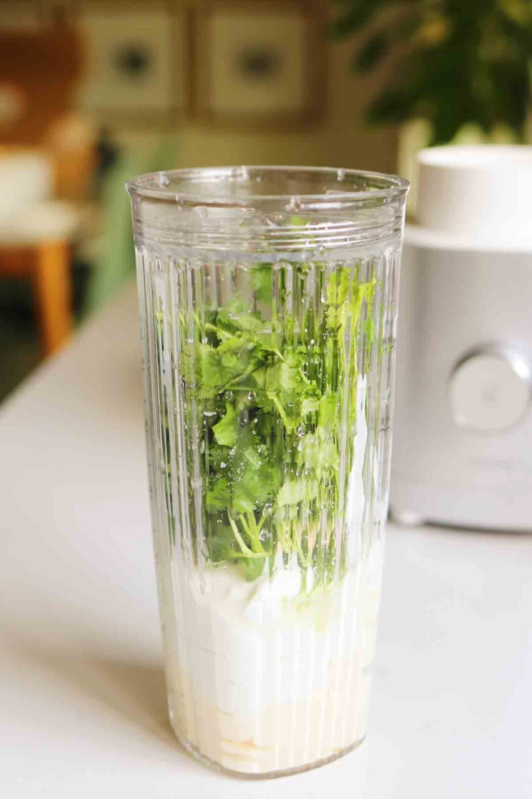 green and white ingredients in a blender cup sitting on a white countertop.