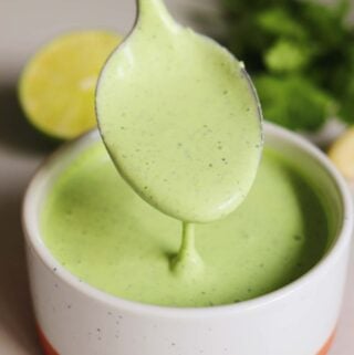 bright green garlic cilantro sauce in a white ramekin with fresh ingredients behind it.