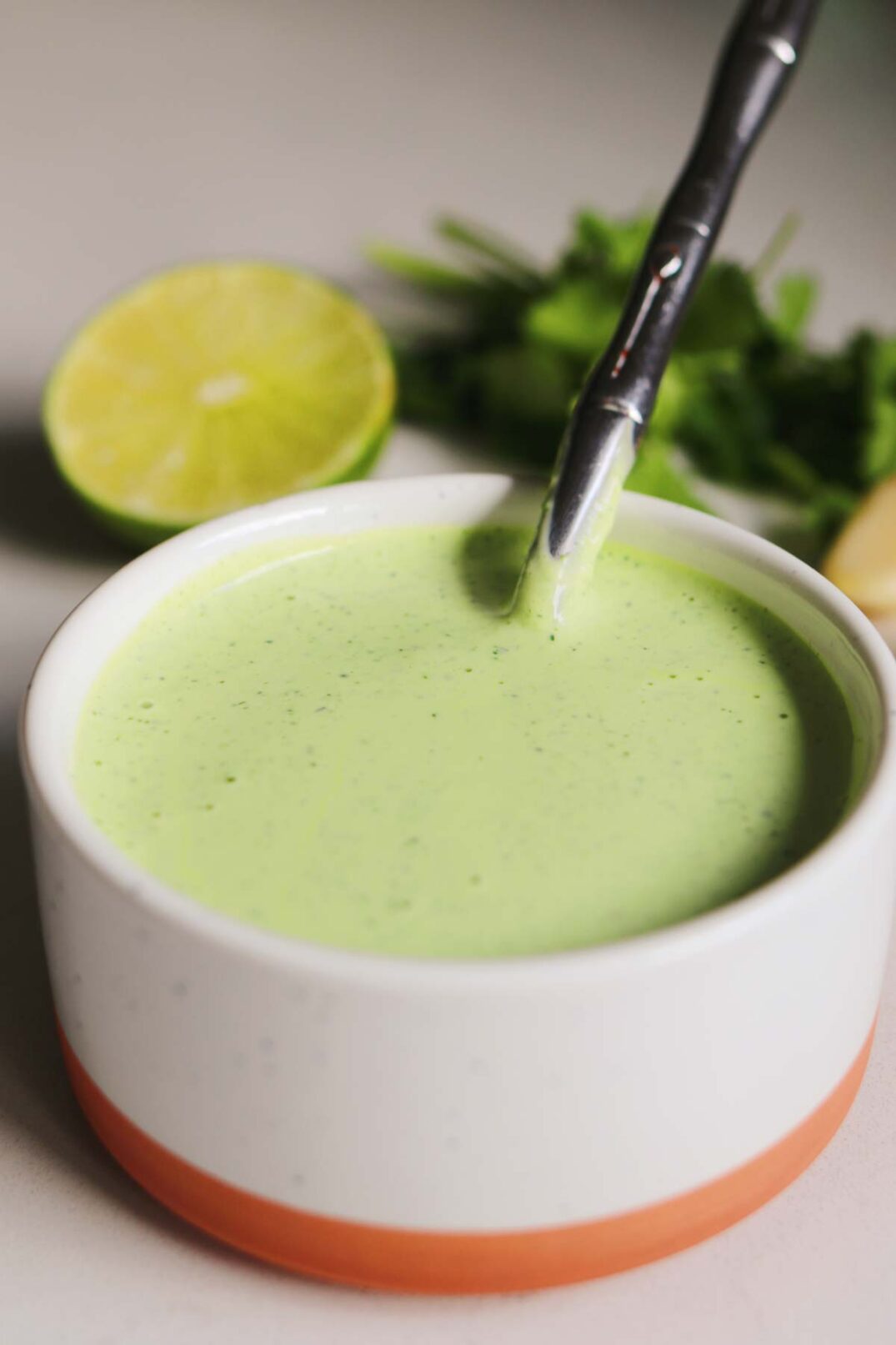 a bright green cilantro garlic sauce in a white bowl with a silver spoon on a white countertop.