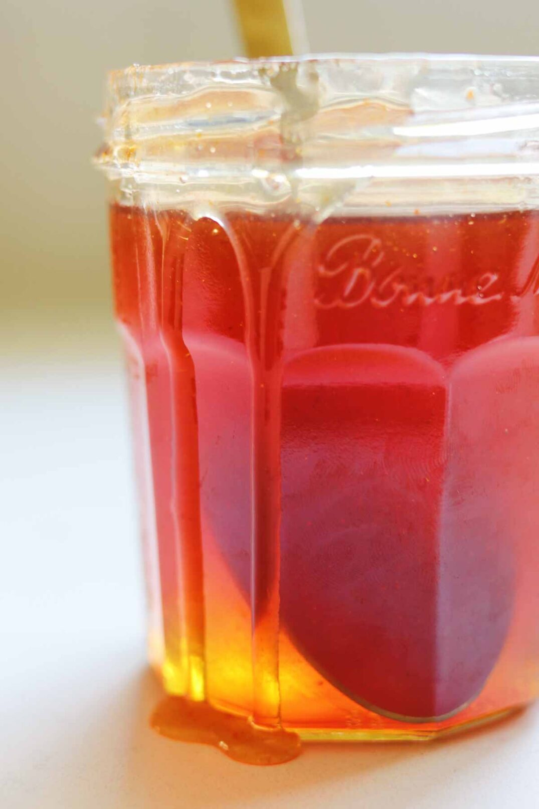a clear jar of hot honey sauce with a drip going down the side. 