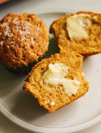pumpkin muffins in a pink muffin tin split open with melted butter.
