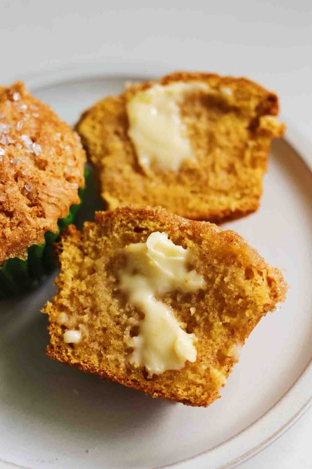 an up close view of a split open pumpkin muffin with melted butter on a white plate. 