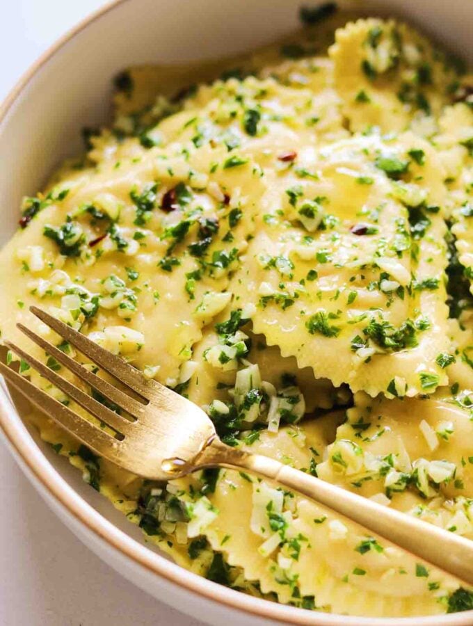 a bowl full of Trader Joe's Cauliflower Ravioli with fresh herbs and a golden spoon.