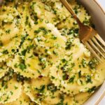 a white our place bowl with a bright green garlic sauce with Trader Joe's Roasted Cauliflower Ravioli.