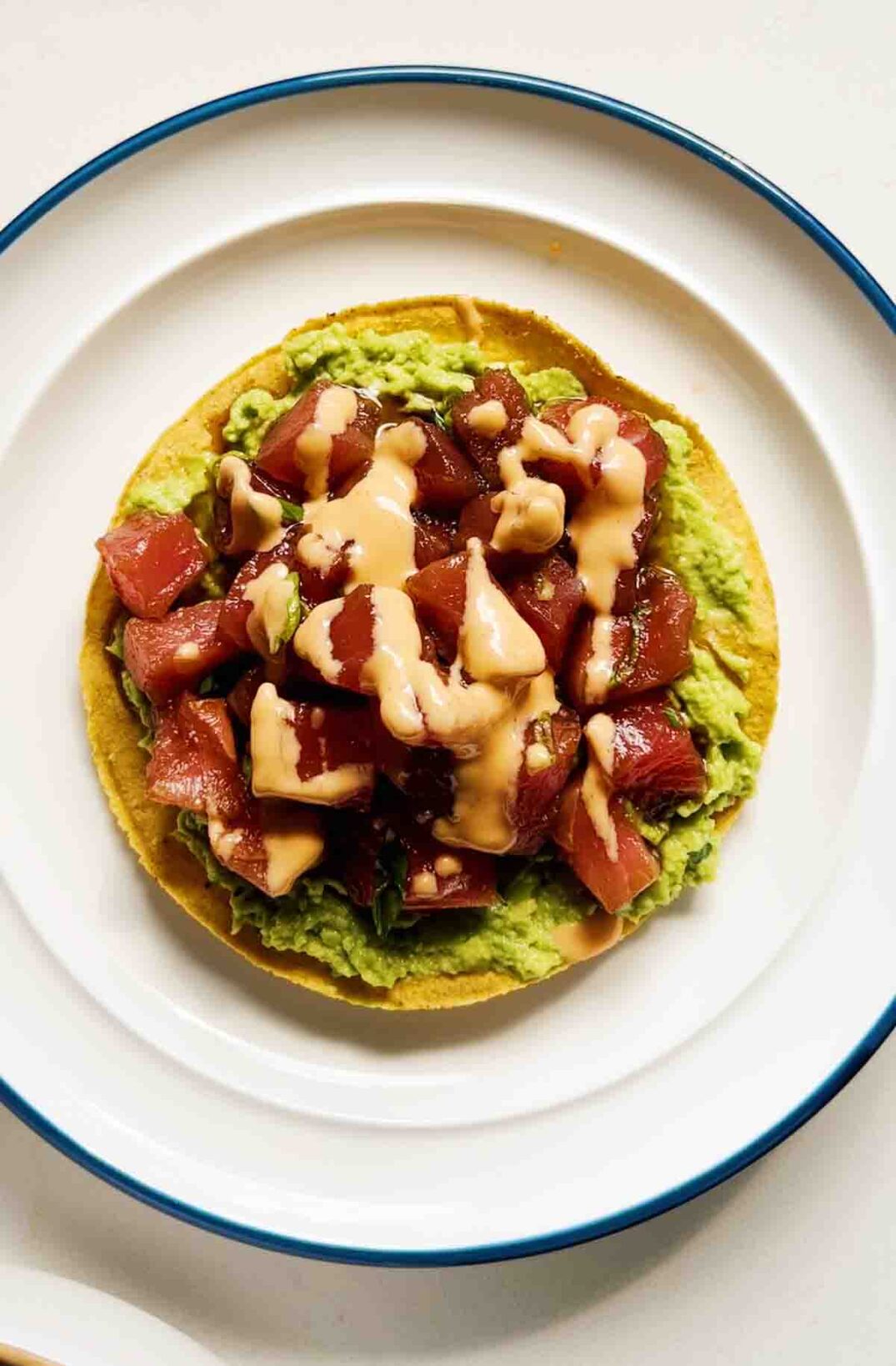 an overhead view of a singular tuna tostada with smashed avocado and spicy mayo.