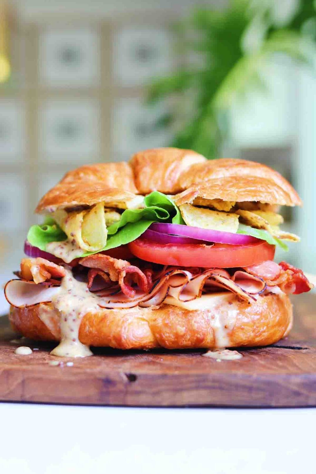 a hero shot of a beautifully styled turkey croissant sandwich on a wooden cutting board. 