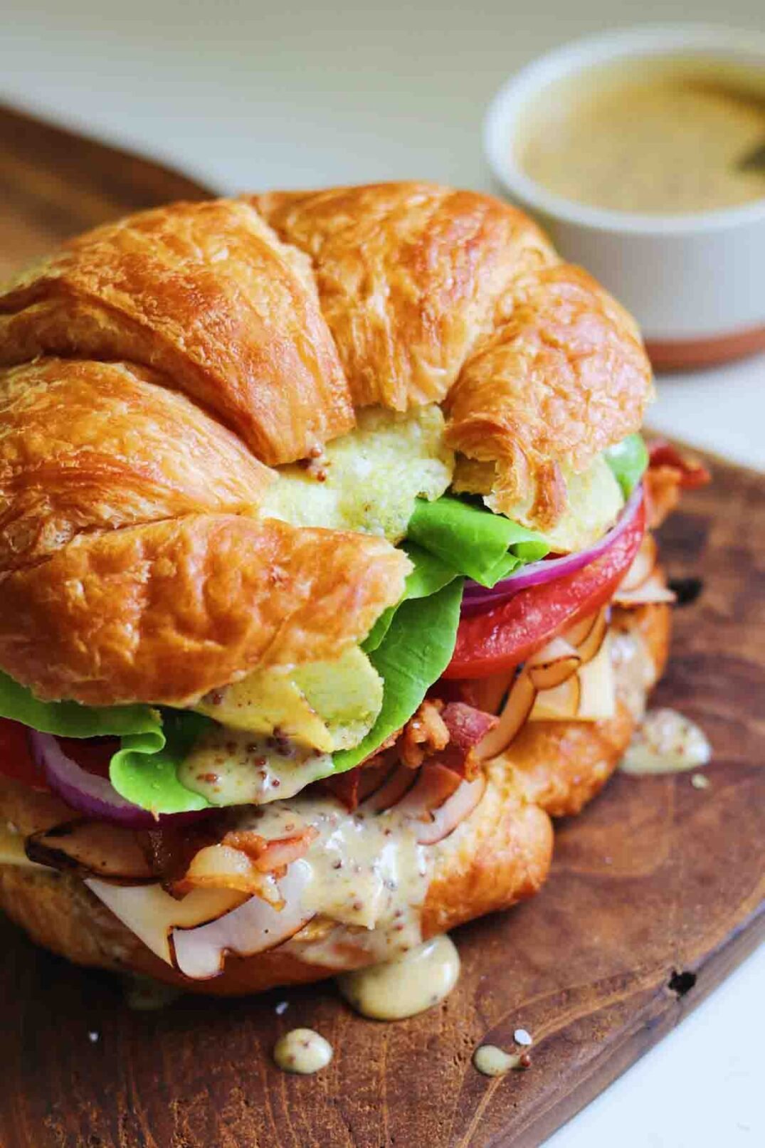 a croissant stuffed with turkey, tomato, lettuce and more on a white plate with honey mustard in the background.