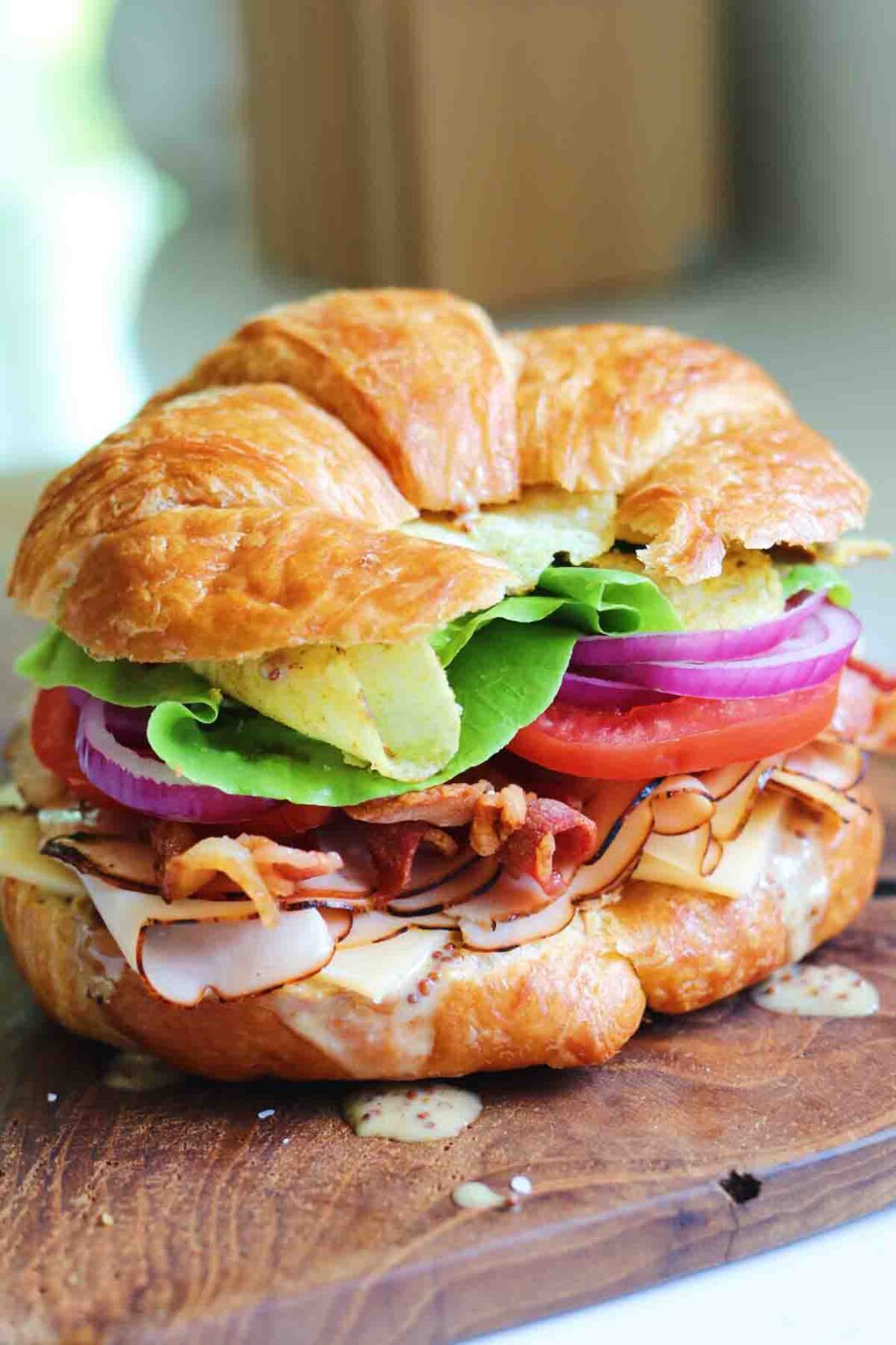 a side view of a perfectly colorful turkey sandwich built on a croissant with honey mustard and veggies.