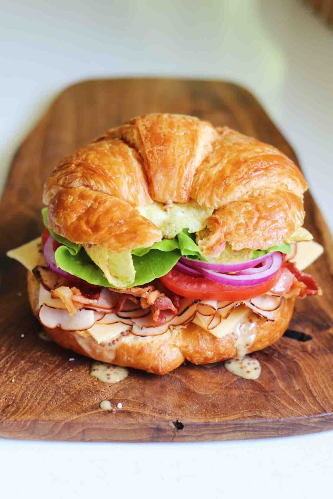a bright and colorful turkey croissant sandwich on a wooden cutting board. 