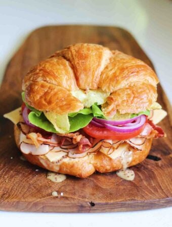 a bright and colorful turkey croissant sandwich on a wooden cutting board.