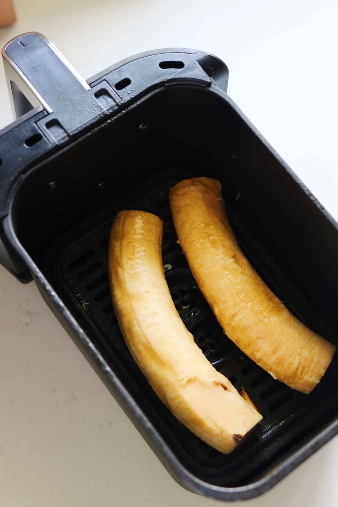 two plantains in an air fryer basket.