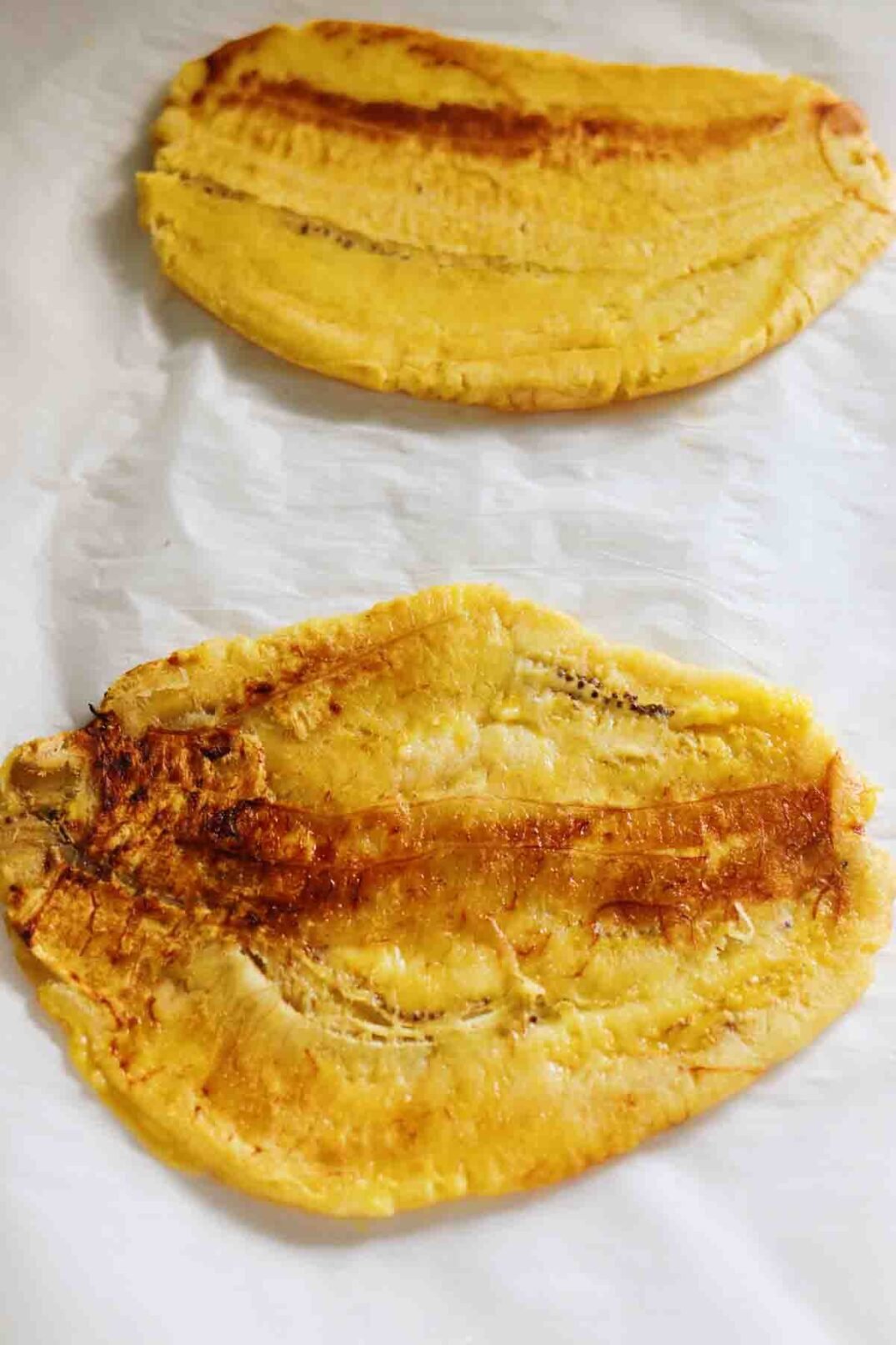 smashed plantains on a sheet of parchment paper.