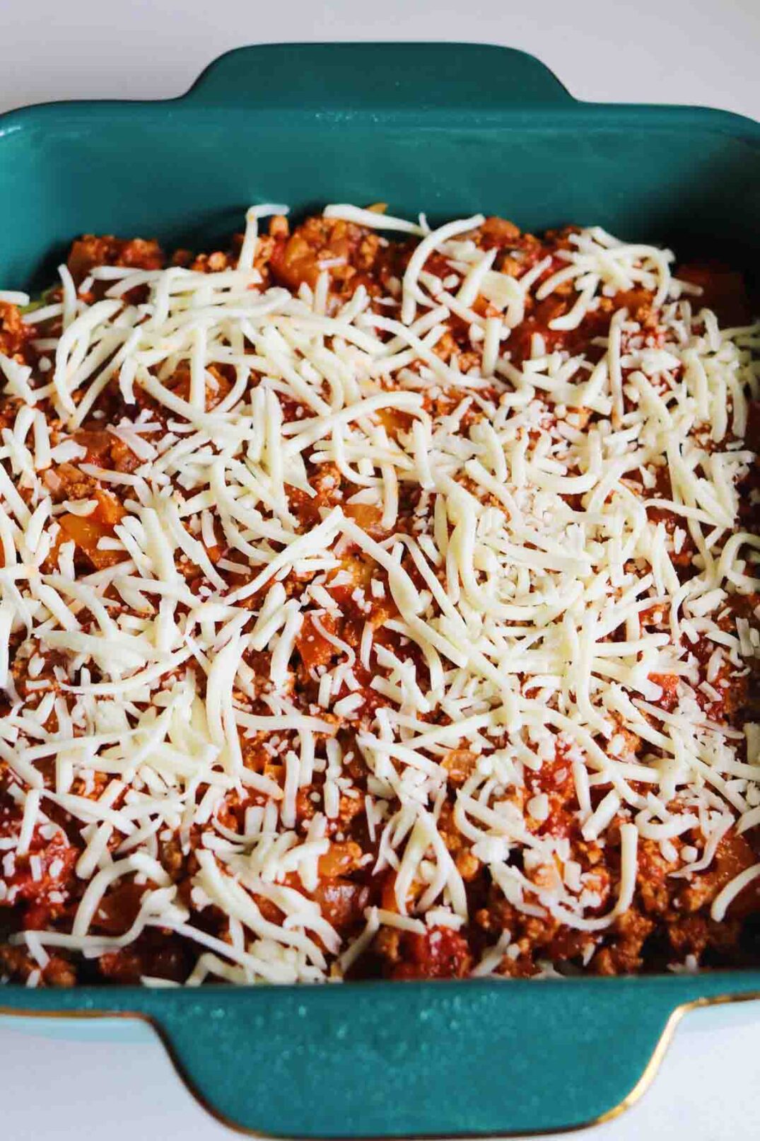 a blue baking dish full of turkey pastelon ingredients with shredded cheese on top.