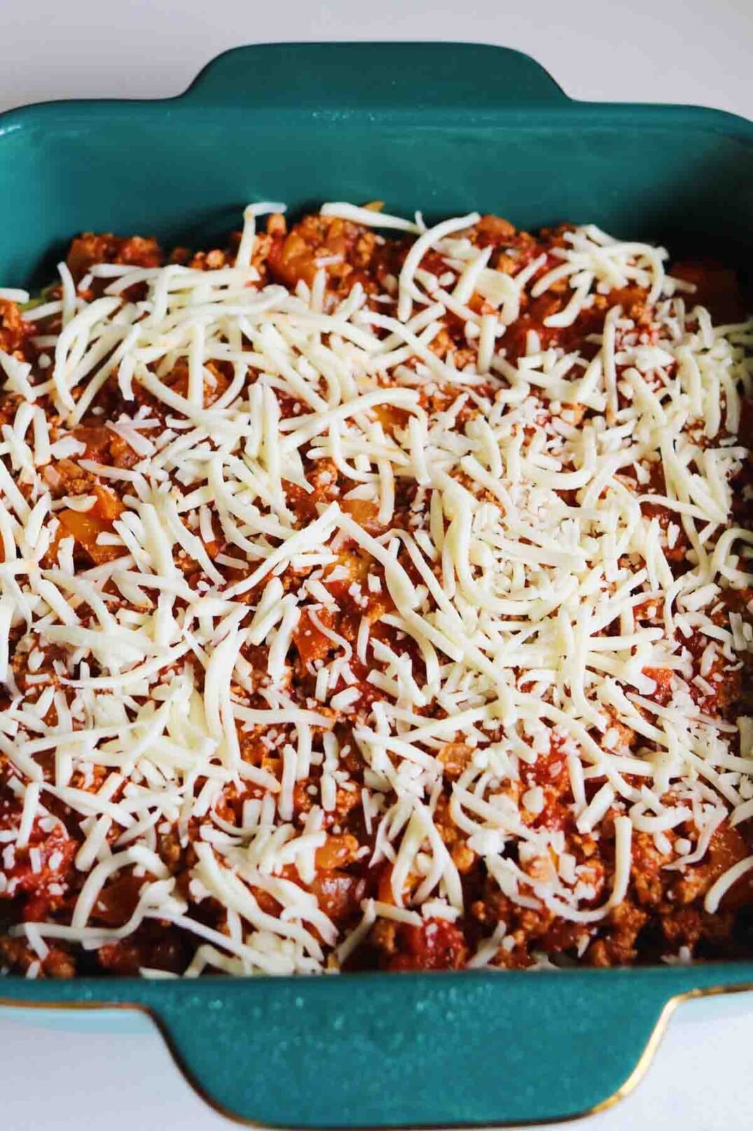 a blue baking dish full of turkey pastelon ingredients with shredded cheese on top. 