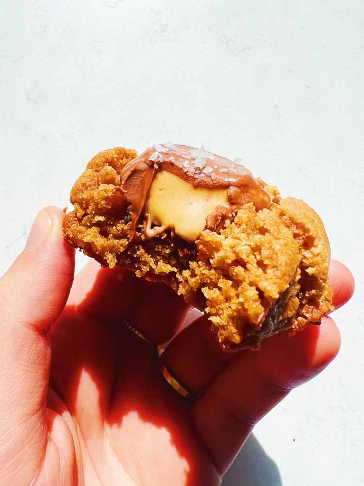 a hand holding a 4 ingredient peanut butter cookie that's bitten into.