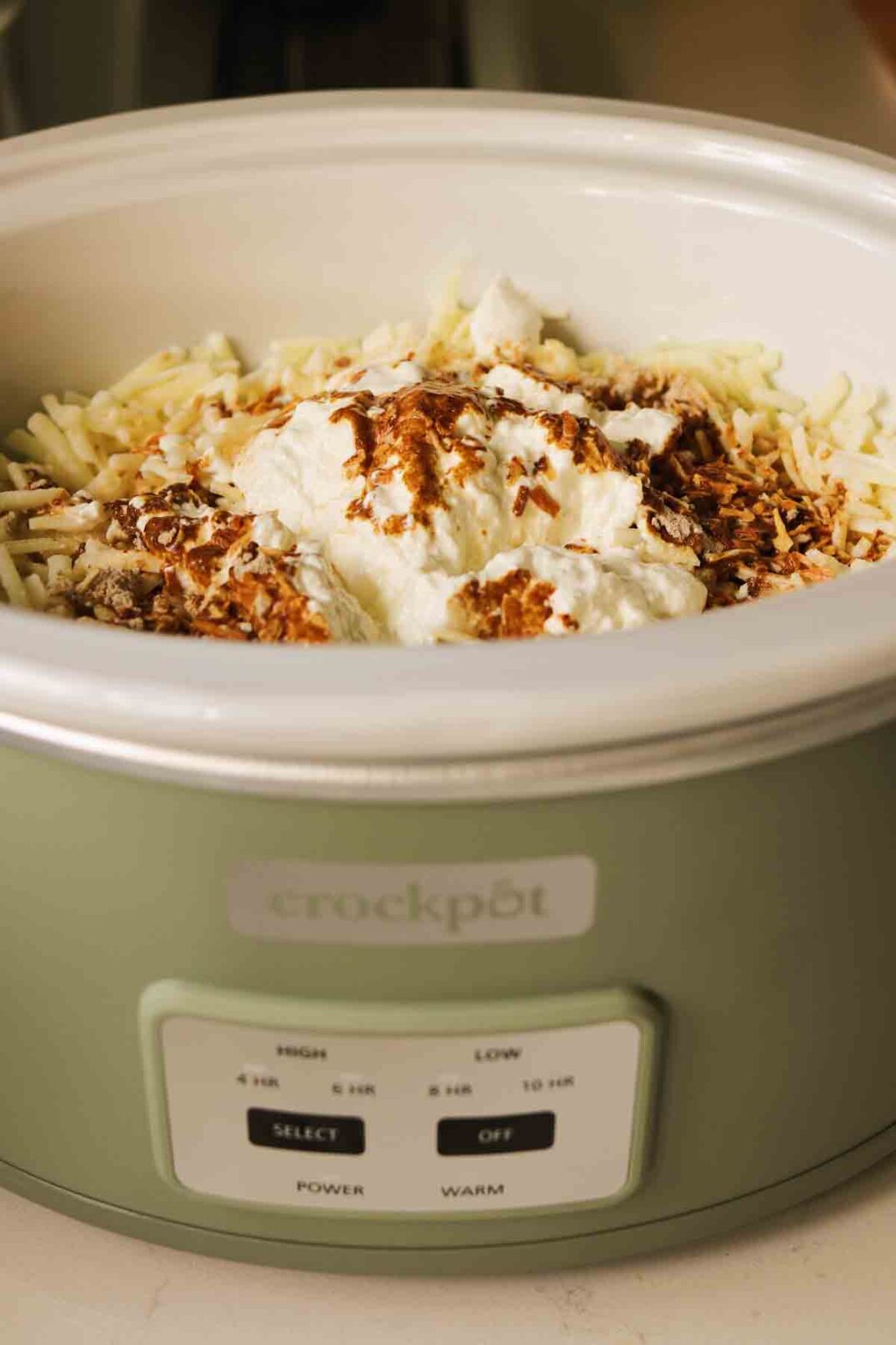 a crockpot being filled up with potatoes, sour cream, cheese, thyme and french onion soup mix.