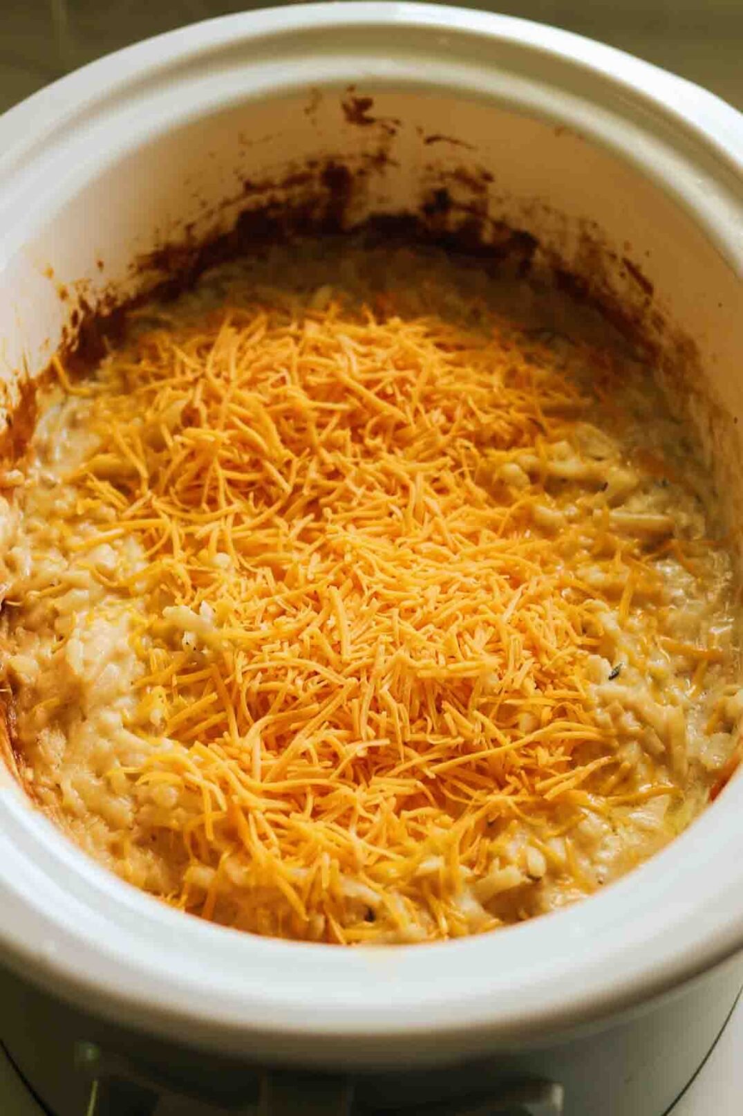 sharp cheddar being poured on top of potatoes in a crockpot. 